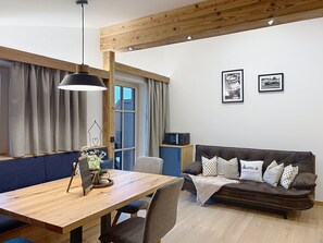 Ein gemütliches Wohnzimmer mit einem Holzesstisch, einer Couch mit Kissen, einem Fernseher und gerahmten Bildern an der Wand.