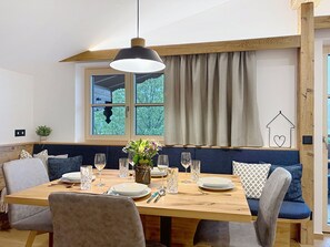 A dining area with a wooden table set for four, surrounded by chairs, with a hanging light fixture above. - Thorermartlgut incl. Gästekarte by Interhome (Saalfelden am Steinernen Meer)