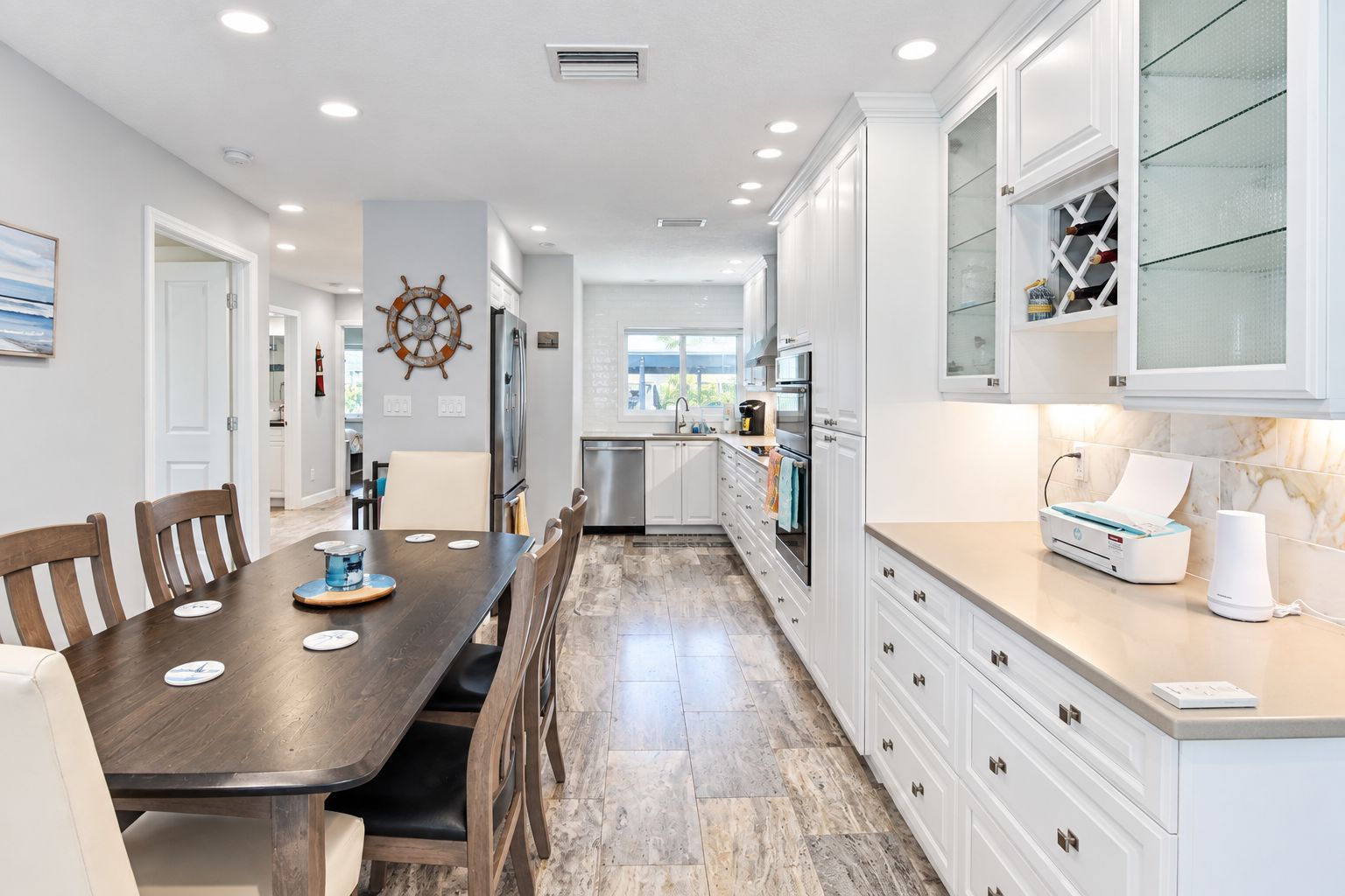 A modern kitchen with white cabinetry, a wooden dining table, and a view to the outside.