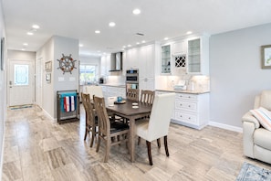 A modern kitchen with white cabinetry, a dining area with a wooden table and chairs, and a light-colored floor. - Longboat Key Condo with Beach Access - Pier Pressure (Longboat Key)