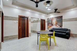 A hotel room with a dining table, yellow chairs, a black sofa, and a Buddha painting on the wall. - Classic Puri Sea Side (Puri)