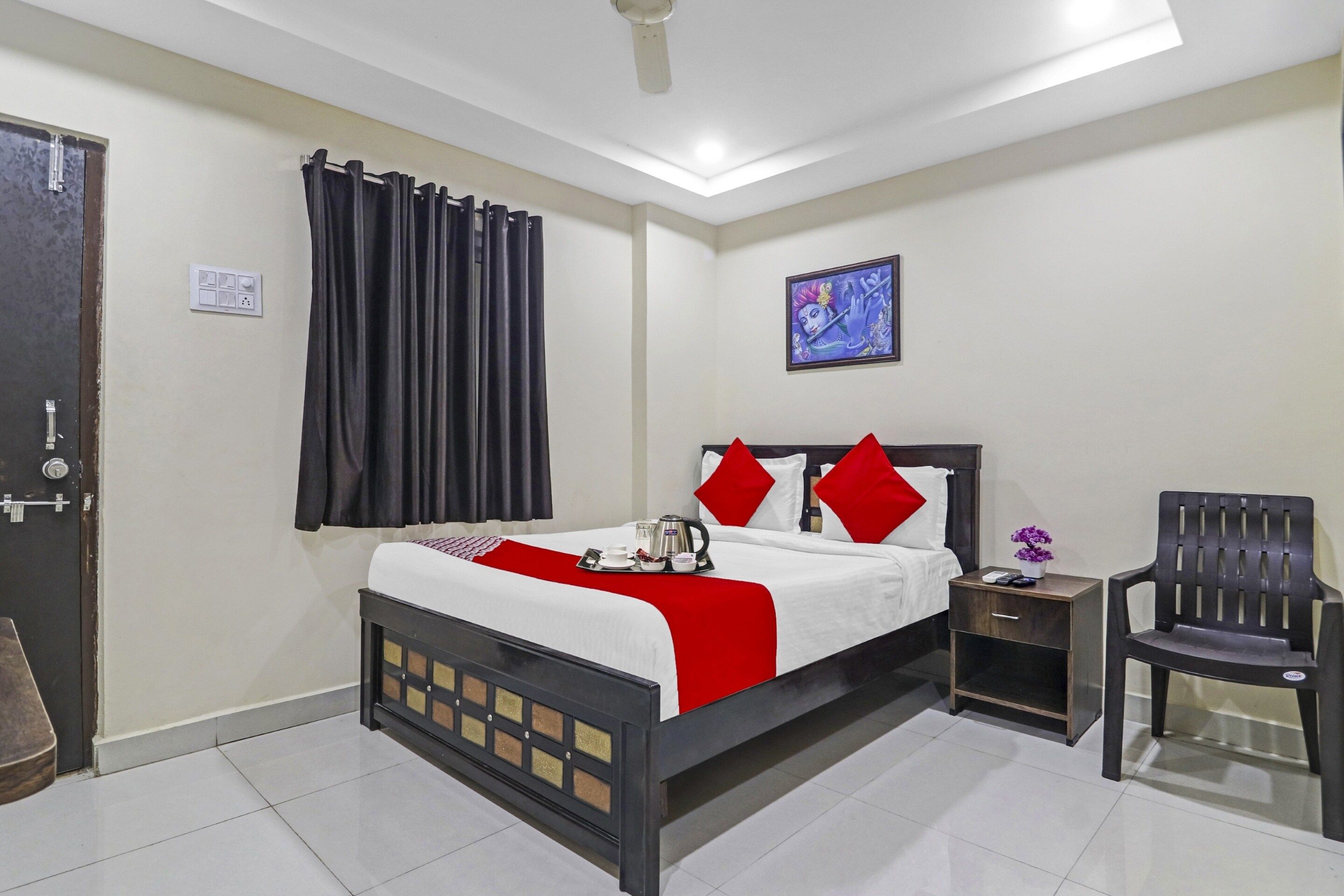 Une chambre d’hôtel comprenant un lit, une table de chevet, une chaise, un ventilateur de plafond et un tableau accroché au mur.