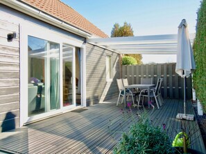 Eine überdachte Terrasse mit Tisch und Stühlen, eine Schiebetür und ein Holzboden.
