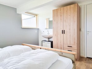 Ein Schlafzimmer mit einem Bett, einem Holzschrank, einem Nachttisch, einem Spiegel und einem Fenster.