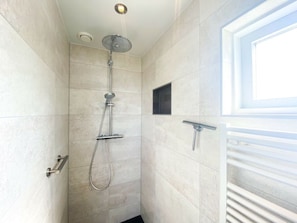 Eine Dusche mit Duschkopf, Wandarmatur und kleinem Fenster.