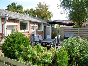 Ein Ziegelhaus mit Terrasse, einem Tisch mit Stühlen und einem überdachten Bereich mit Sonnenschirm.