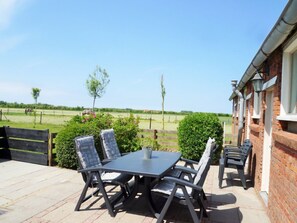 Eine Terrasse im Freien mit Tisch und Stühlen, ein Backsteinhaus und Blick auf ein Feld mit Bäumen und einem Zaun.