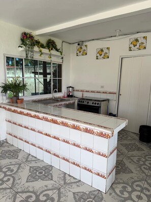 A kitchen with a central island, a stove, and a sink. - Beach Getaway in El Zapote - 3BR Home with AC (El Zapote)