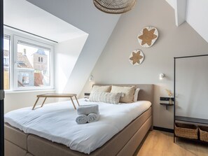 Ein modernes Schlafzimmer mit schrägen Wänden, einem Bett mit weißen Leinen, einem Nachttisch aus Holz und zwei Stern-Dekorationen an der Wand.