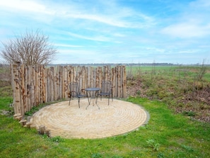 A circular brick patio with two metal chairs and a table, surrounded by a wooden fence. - Holiday Home With 2 Bedrooms (Den Hoorn)