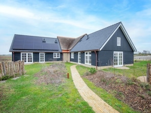A two-story house with a dark exterior, a sloped roof, and a paved driveway leading to the entrance. - Holiday Home With 2 Bedrooms (Den Hoorn)