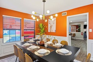 Ein Esszimmer mit einem schwarzen Tisch, gedeckt für sechs Personen, orangefarbenen Wänden und einem modernen Kronleuchter.