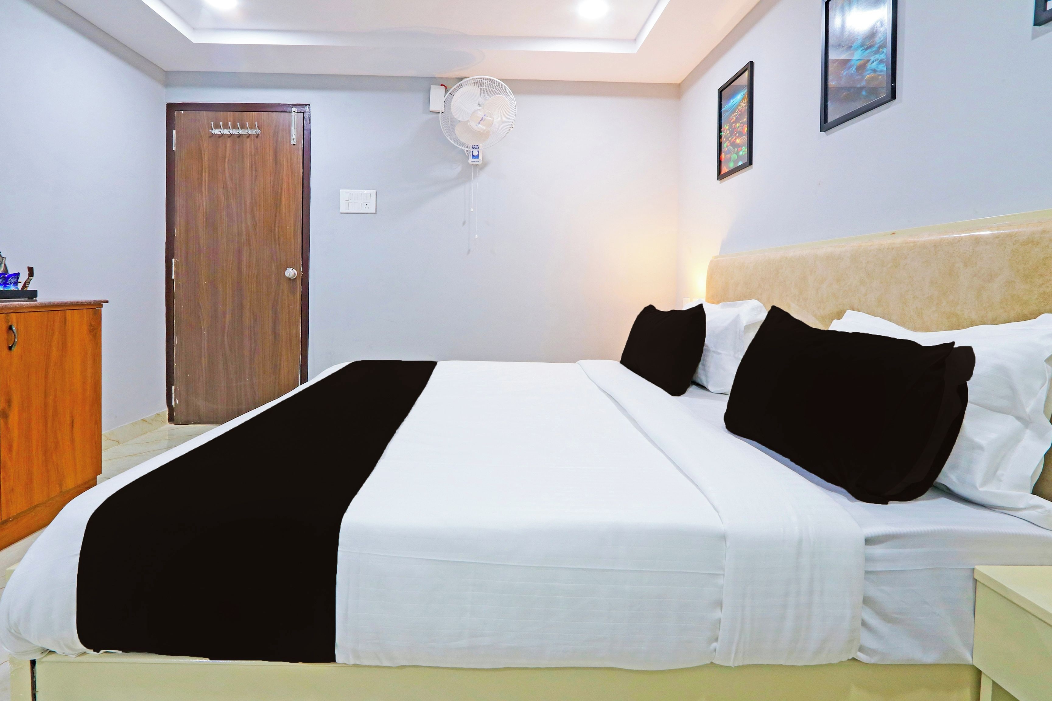 Una habitación de hotel con cama, armario de madera, ventilador de techo e iluminación en la pared.