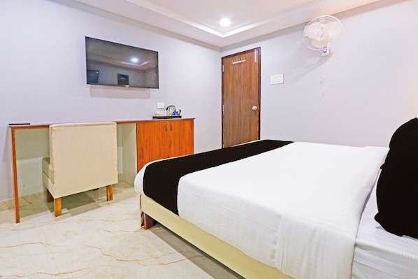 Un dormitorio con cama, escritorio, silla, armario y televisor en la pared.