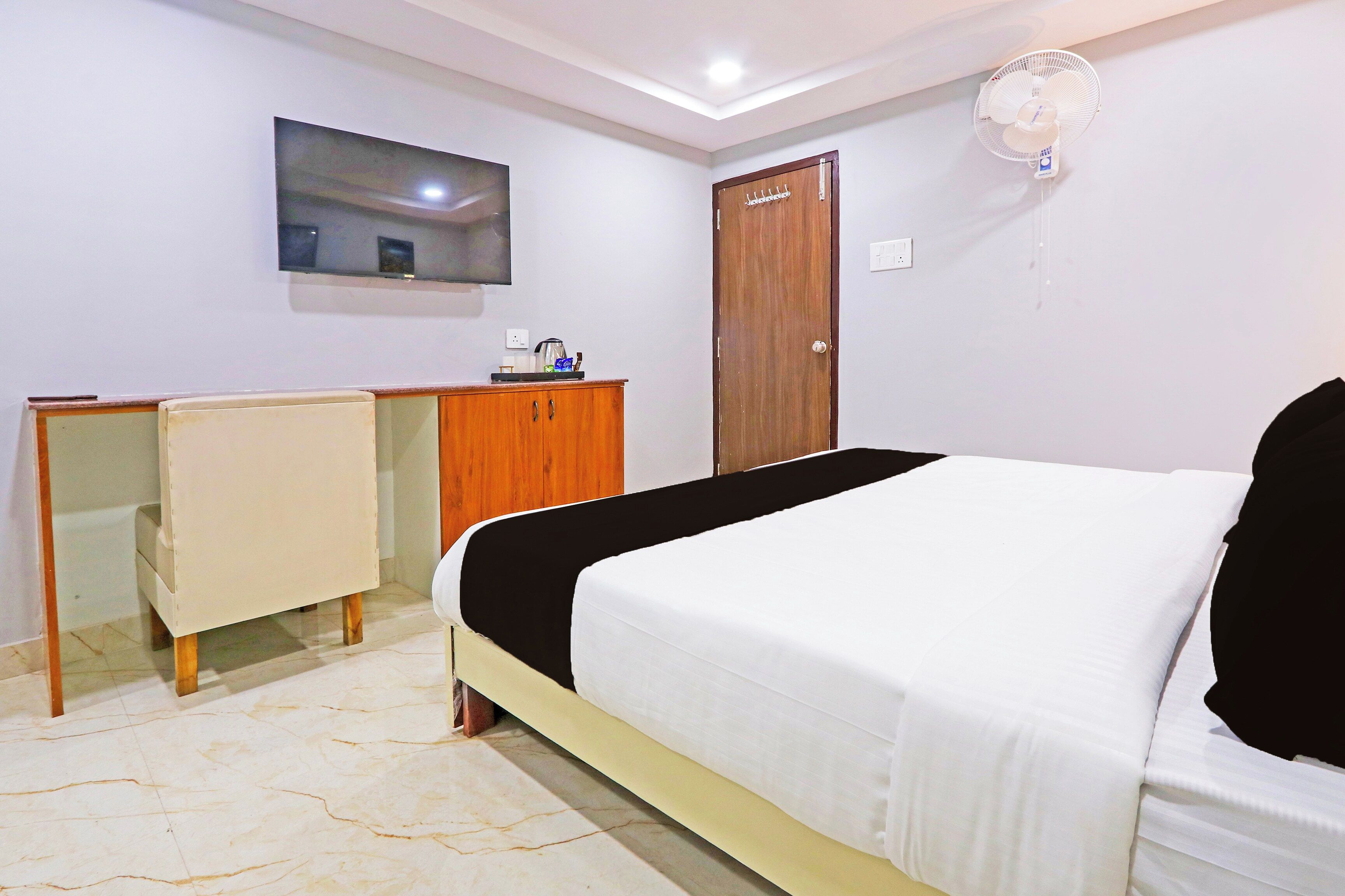 A bedroom with a bed, a desk, a chair, a wardrobe, and a television on the wall.
