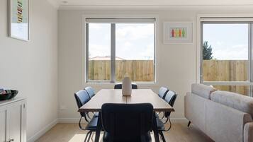 Un comedor moderno con una mesa, sillas, un sofá y ventanas amplias con vista a una cerca de madera.