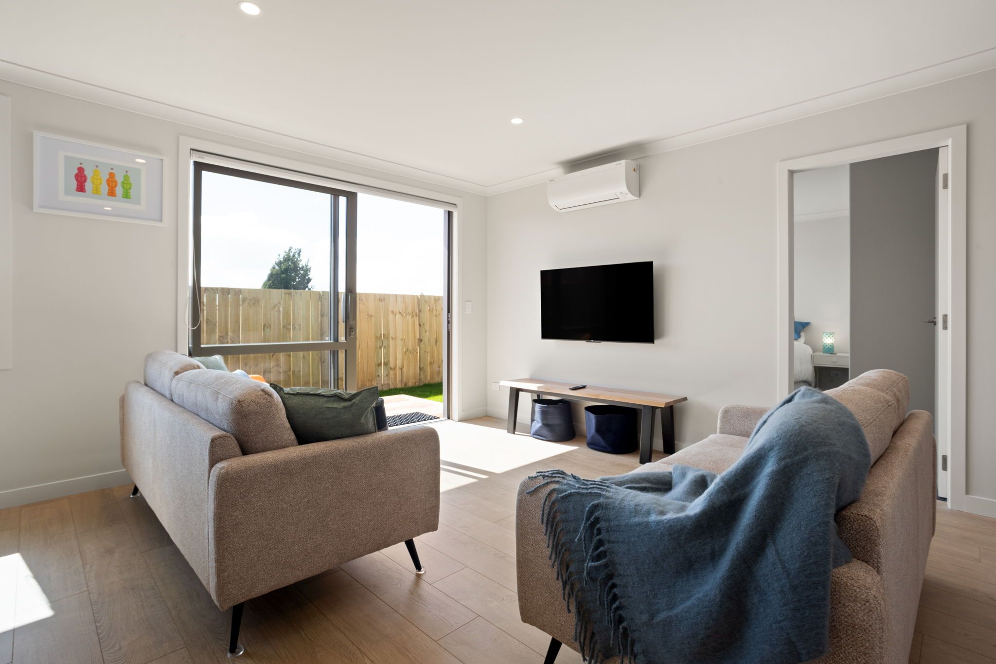 Een moderne woonkamer met twee banken, een flatscreen televisie en een schuifdeur naar een achtertuin.