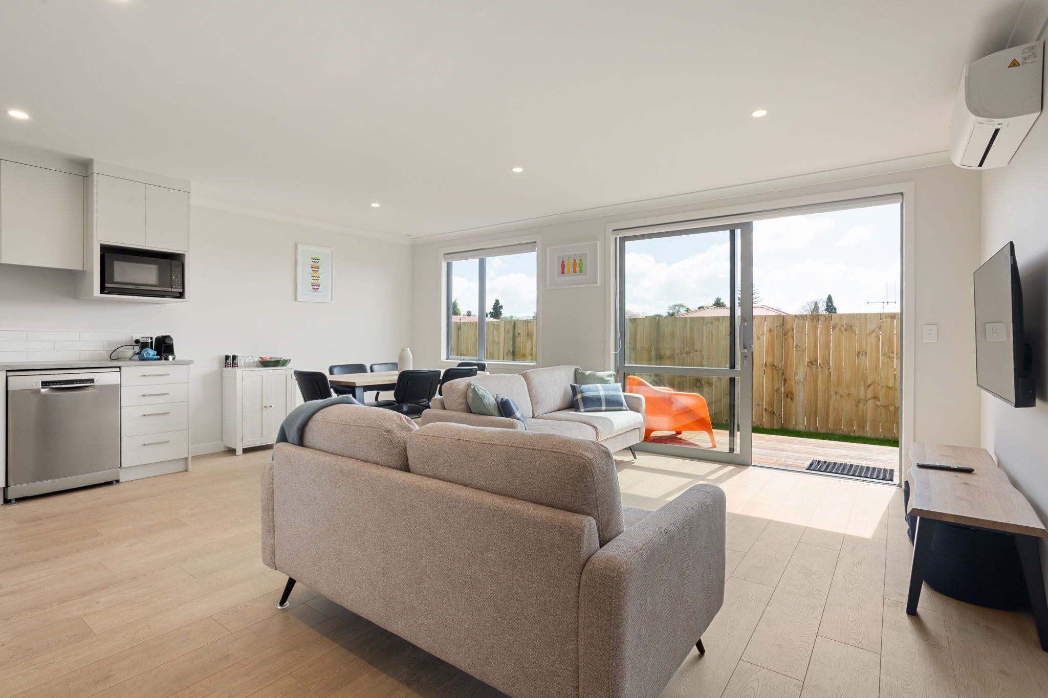 A modern living space with a kitchen, dining area, and a large sliding glass door leading to a patio.