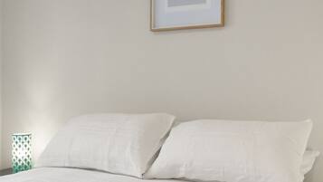 Een slaapkamer met een bed, witte kussens, een inlijsting foto aan de muur en een blauw detail bij het voeteneinde van het bed.