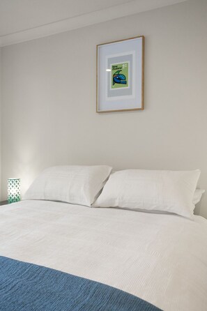 Une chambre à coucher avec un lit, des oreillers blancs, un tableau encadré au mur et un élément décoratif bleu au pied du lit.
