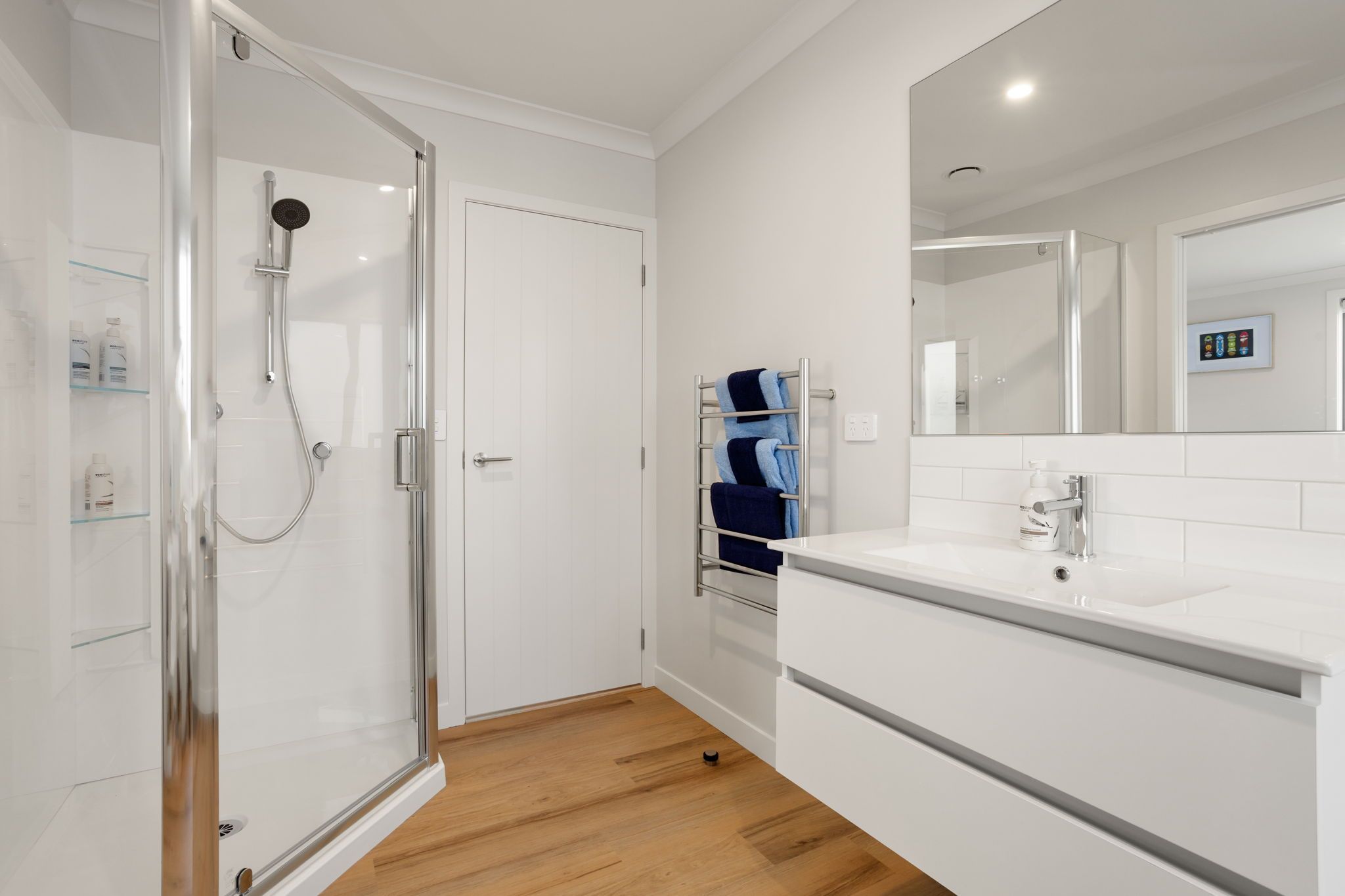 A modern bathroom with a glass shower enclosure, a white sink, and a towel rack.