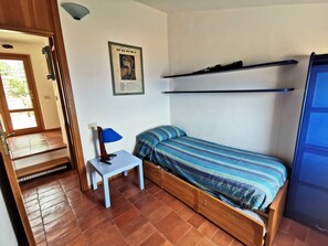 A compact room with a bed, a small table, a wall-mounted shelf, and a poster. - Holiday Home With 2 Bedrooms (Marciana)
