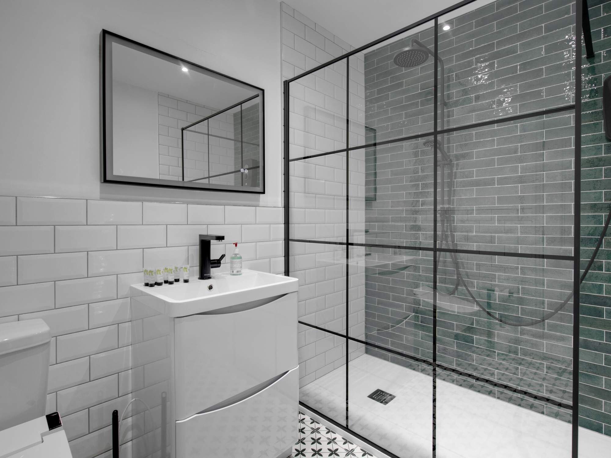 Een moderne badkamer met een glazen douchecabine, witte betegelde wanden en een wit wastafelmeubel met toiletartikelen.
