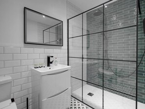 Une salle de bain moderne avec une douche à parois de verre, des murs recouverts de carrelage blanc et un lavabo blanc agrémenté d’articles de toilette.