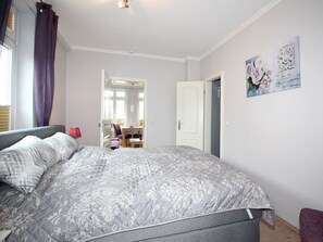 A bedroom with a bed, a desk, and a chair. There is a door leading to another room. - Holiday Apartment in Sylt With 2 Bedrooms (Sylt)