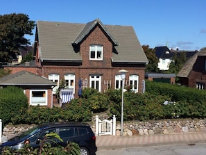A two-story brick house with a gabled roof, a front porch, and a stone wall. - Holiday Apartment in Sylt With 2 Bedrooms (Sylt)