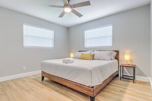 Un dormitorio con cama, dos lámparas de noche, ventilador de techo y dos ventanas con persianas.