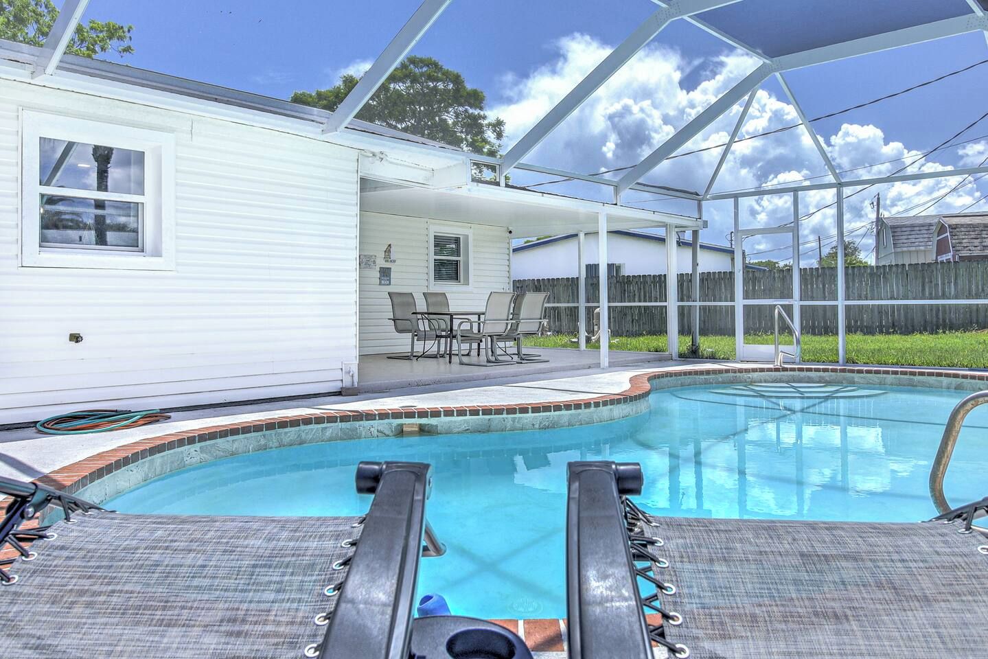 A swimming pool with a covered patio area, a fenced backyard, and a white house.