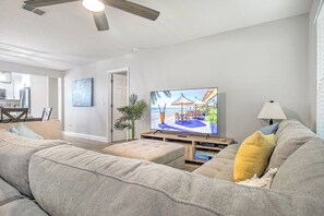 Una sala de estar con un sofá grande, una televisión y un comedor al fondo.