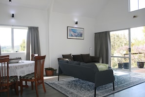 A living room with a sofa, chairs, a dining table, and a large window. - Cozy Stay on Coast to Coast (Kaikohe)