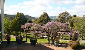 Ein Garten mit blühenden Bäumen, einem Ziegelweg und Blick auf ferne Hügel.