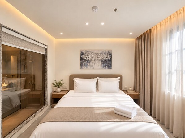 A modern hotel room with a large bed, a glass-enclosed shower area, and a cityscape painting on the wall.