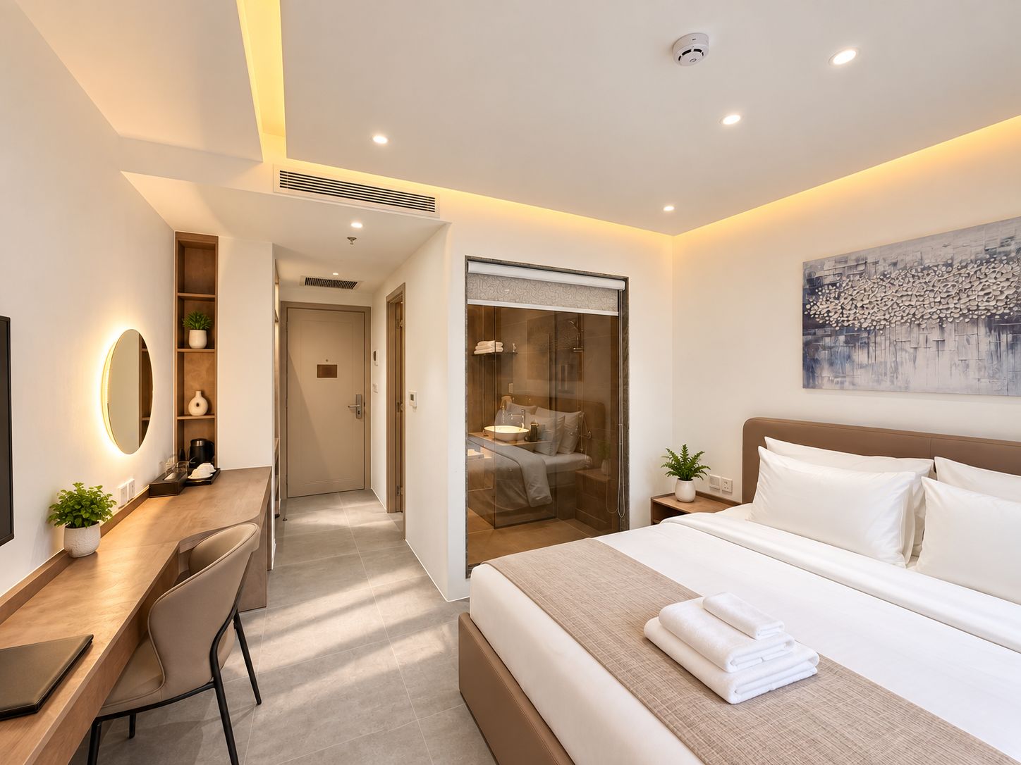 A modern hotel room with a bed, desk, chair, and a large painting on the wall.