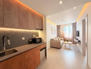A modern kitchen with a built-in oven, a sink, and a microwave. There is a dining area with a sofa and a small table.
