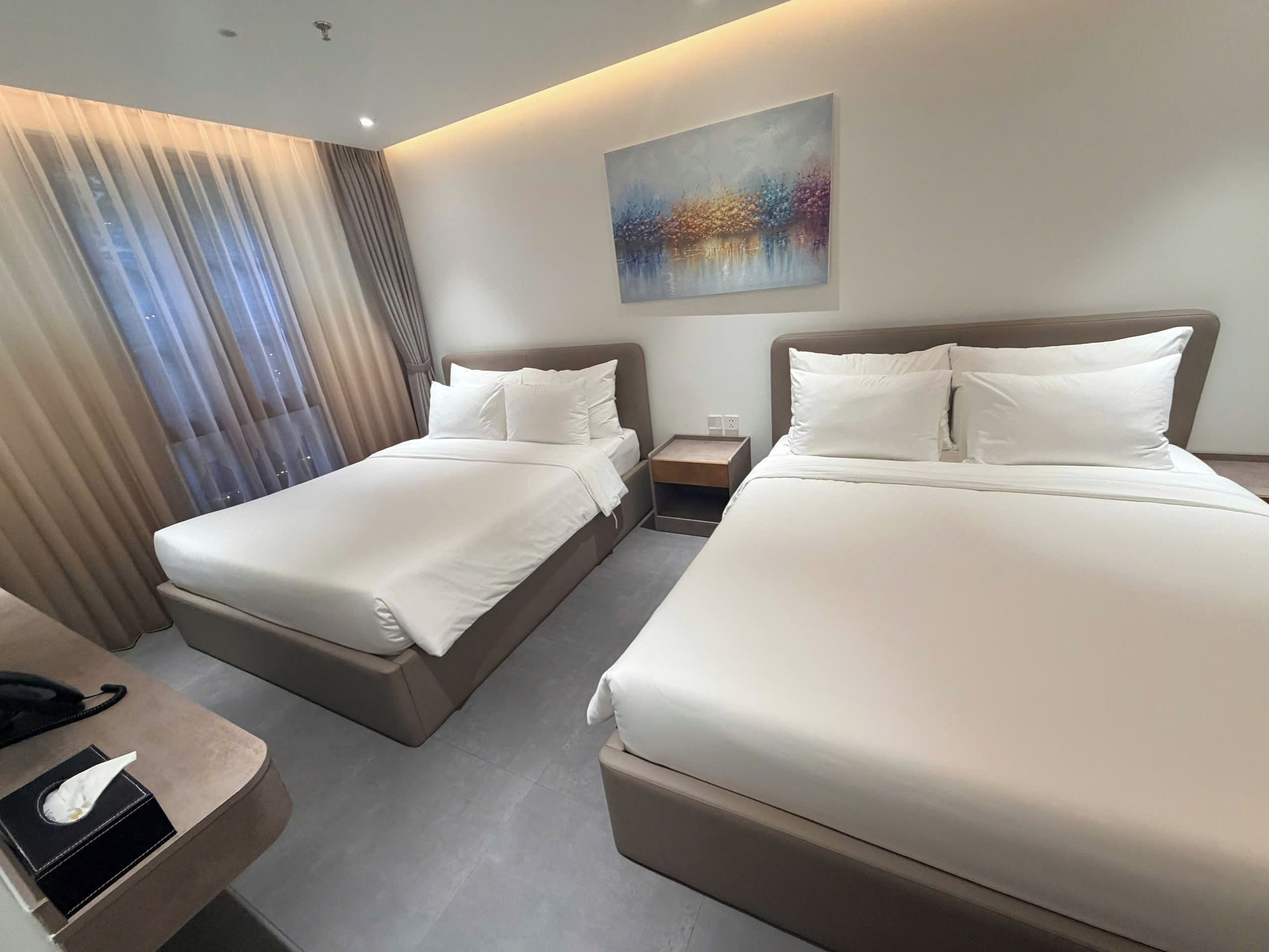 Habitación de hotel con dos camas, una mesita de noche, un cuadro y una ventana con cortinas.