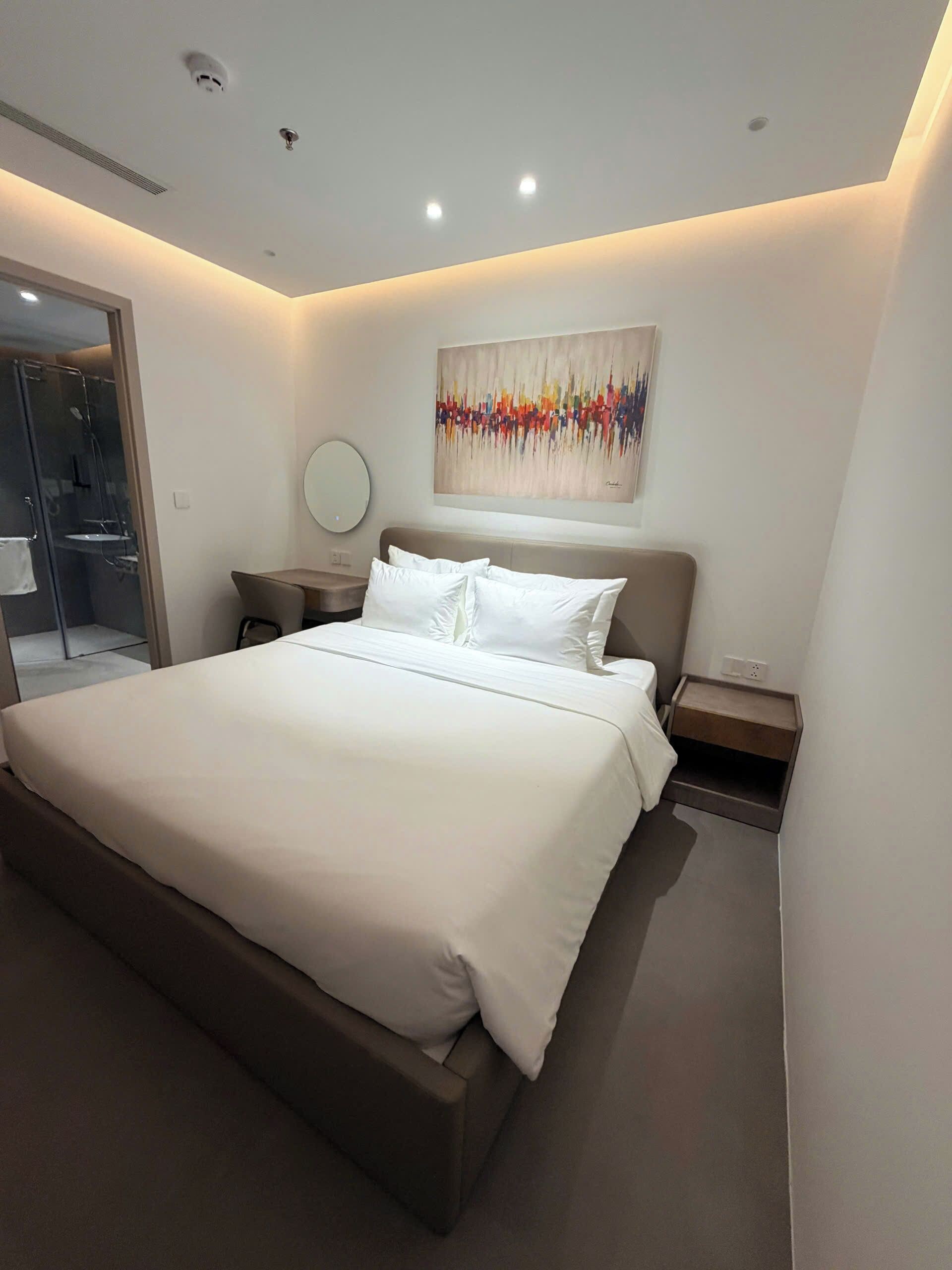 Un dormitorio moderno con una cama grande, una mesita de noche, un espejo redondo y una obra de arte colgada en la pared.