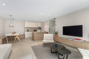 A modern living room with a flat-screen TV, a coffee table, a sofa, and a dining area with a table and chairs. - 2-bedroom Zeedijk Apartment (Blankenberge)