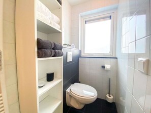 Ein Badezimmer mit Toilette, Ablagefläche für Handtücher, Toilettenpapierhalter und einem Fenster.