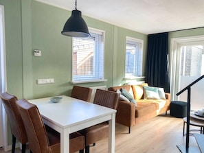 Ein Essbereich mit einem weißen Tisch und braunen Stühlen, einer Couch mit Kissen sowie einer schwarzen Pendelleuchte.