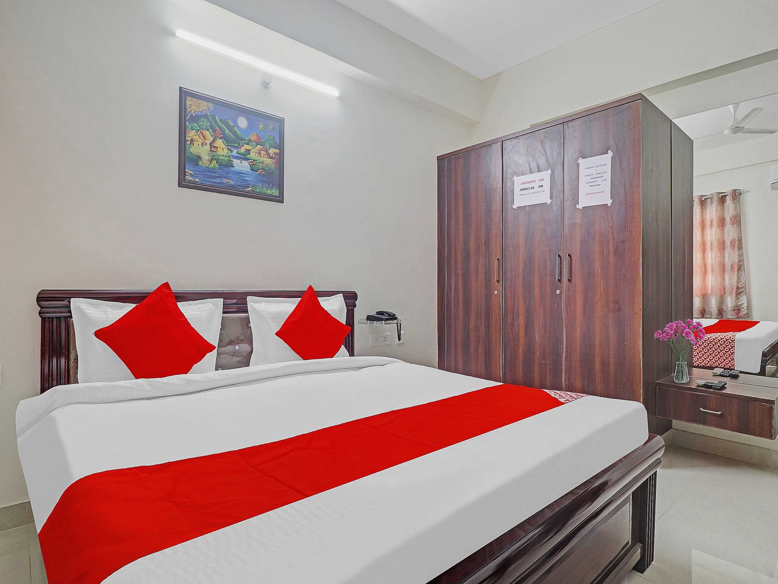 Habitación de hotel con cama, armario, escritorio con un florero y un cuadro en la pared.