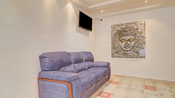 Una habitación con un sofá púrpura, un televisor montado en la pared y una estatua de Buda.