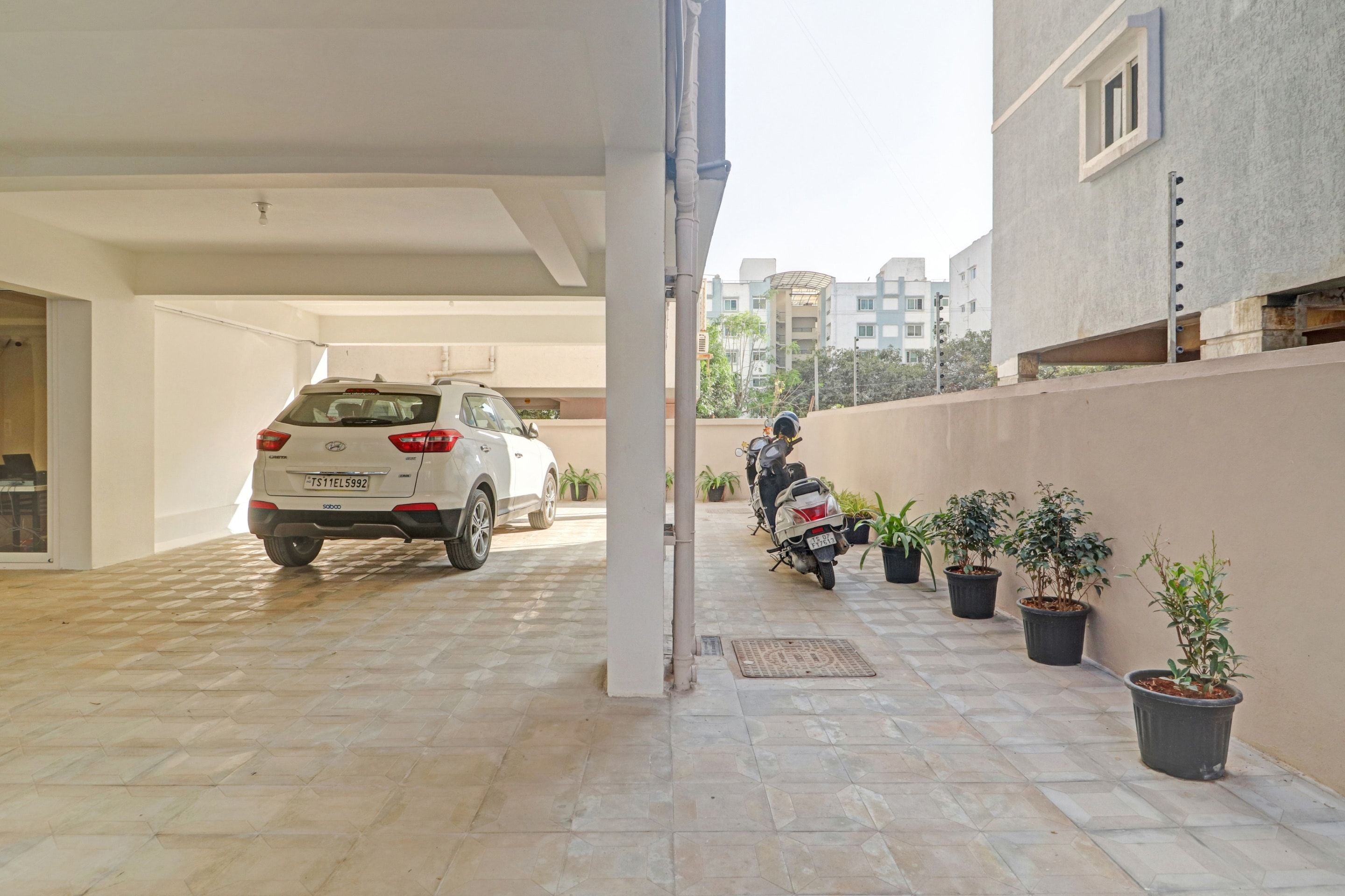 Un espace de stationnement couvert où sont garés un VUS blanc et une moto. Des plantes en pot sont disposées le long du mur.