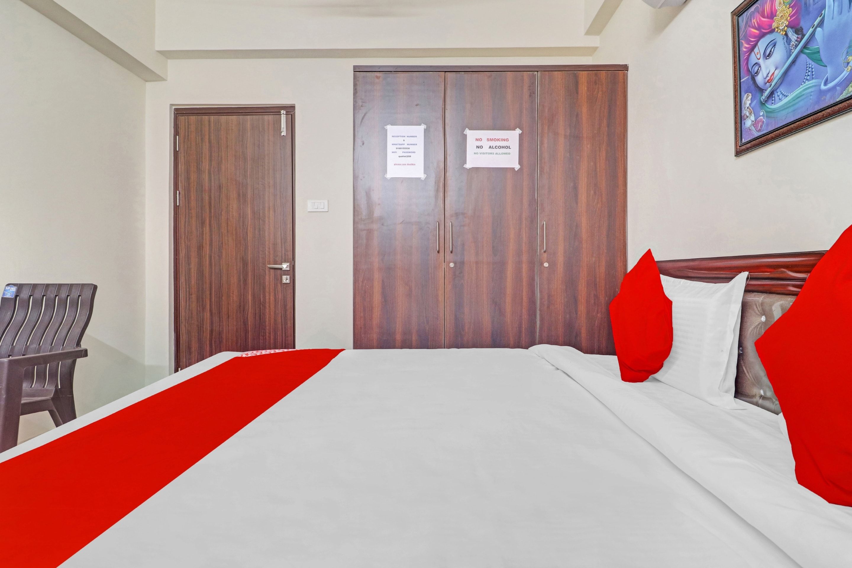 Habitación de hotel con cama, armario de madera, una silla y un cuadro colgado en la pared.