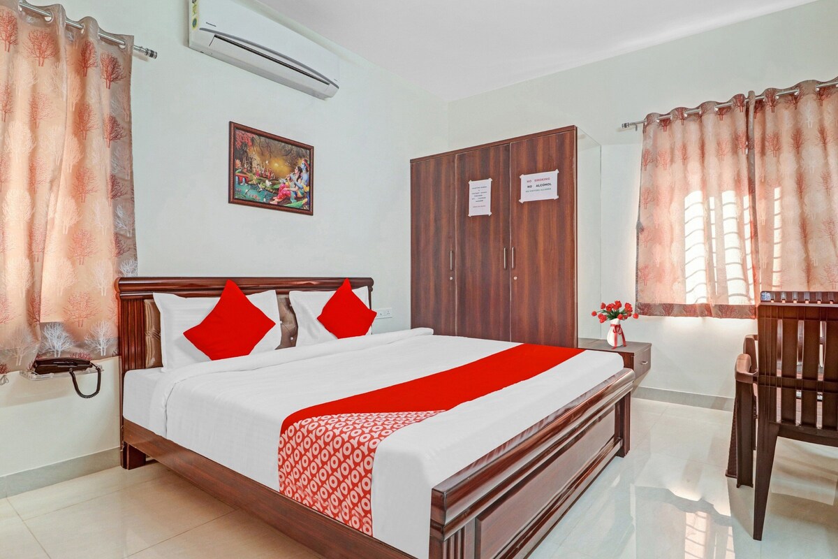 Habitación de hotel con cama, armario, escritorio y silla. Hay un cuadro en la pared y un aire acondicionado sobre la cama.