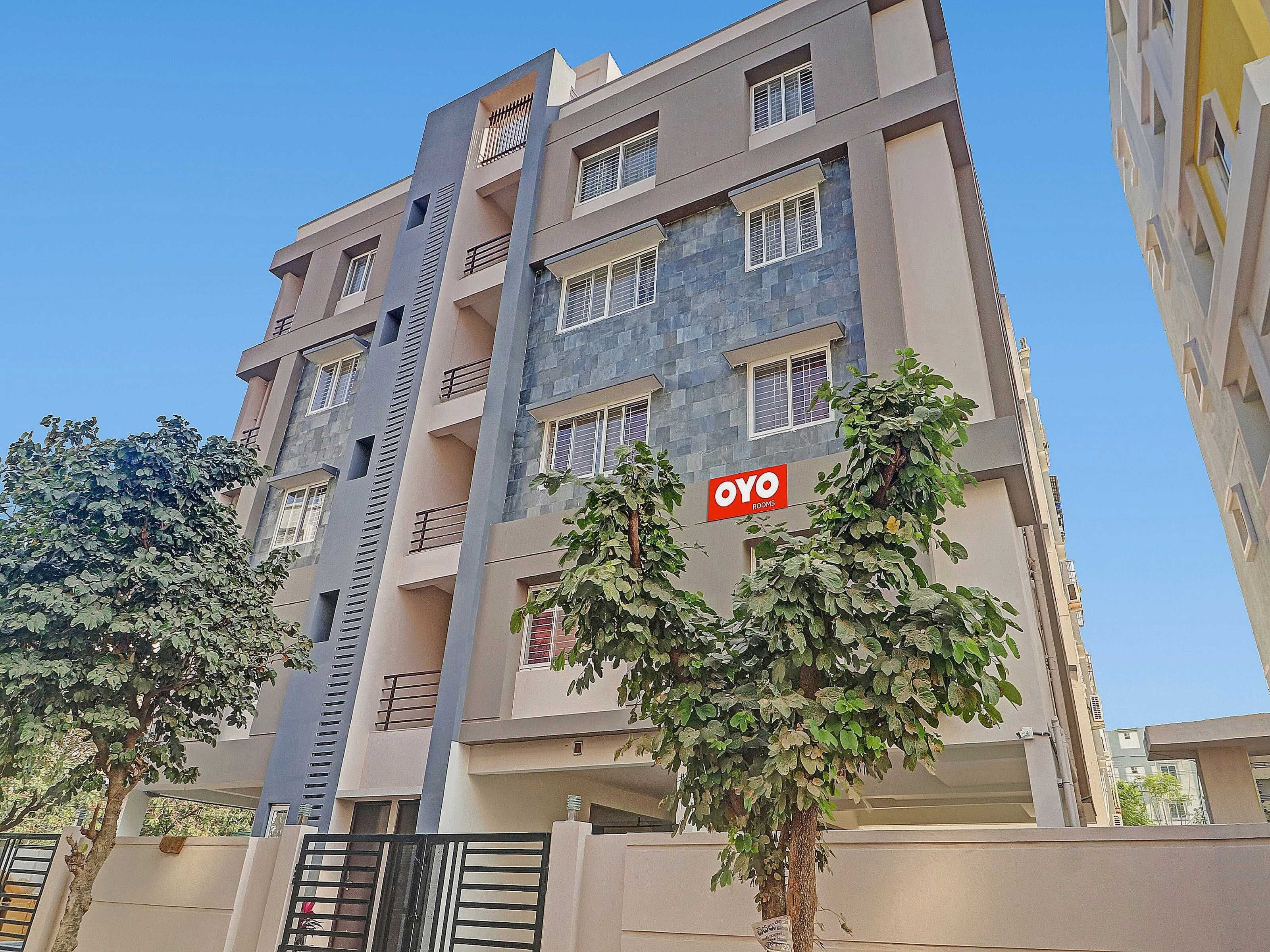 A multi-story building with balconies, a sign for 'OYO Rooms,' and a tree in front.