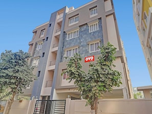 Un edificio de varios pisos con balcones, un letrero que dice 'OYO Rooms' y un árbol en frente.